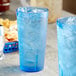 Two blue Choice plastic tumblers filled with ice on a table with a basket of food.