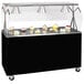 A black and silver Vollrath portable buffet cart with a clear cover over a black counter top with cupcakes displayed.