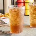 Two Choice clear plastic tumblers filled with iced tea on a table with a basket of fries.