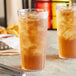 A pair of Choice clear plastic tumblers filled with iced tea on a table.