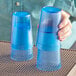 A hand holding two blue Choice plastic tumblers on a table.