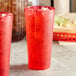 Two red Choice SAN plastic tumblers filled with ice and red liquid on a table.