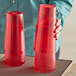 A person holding a stack of red Choice plastic tumblers.
