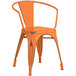 A Lancaster Table & Seating distressed orange metal arm chair with a wooden seat.
