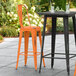 Two Lancaster Table & Seating distressed orange barstools on a patio.