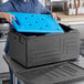 A woman holding a blue CaterGator food pan carrier board in a black plastic box.