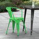 A Lancaster Table & Seating distressed green outdoor arm chair next to a black table on a sidewalk.