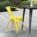 A yellow Lancaster Table & Seating outdoor arm chair on a patio next to a table.
