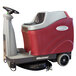 A red and gray Minuteman Max Ride AGM cordless ride-on floor scrubber with wheels and a handle.