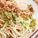 A plate of noodles with white sesame seeds, meat, and green onions.
