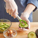 A person using a Choice avocado slicer with a green handle to pit and slice an avocado.