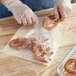 A person wearing plastic gloves holding a clear Choice polyethylene bag with a pretzel inside.
