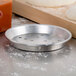 An American Metalcraft silver aluminum pizza pan with holes next to pizza dough on a wooden cutting board.