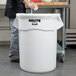 A person putting paper in a white Rubbermaid commercial trash can.