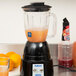 A Waring blender with orange liquid in the jar next to oranges.