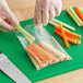 A person cutting a carrot stick in a clear polyethylene layflat bag.
