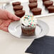A hand holding a cupcake with sprinkles on a Vollrath stainless steel plate.
