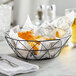 A Tablecraft black stainless steel wire serving basket of food and a glass of beer.