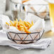 A Tablecraft black stainless steel wire serving basket holding french fries.