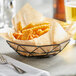 A Tablecraft black stainless steel wire serving basket filled with fries on a table.