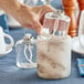 A hand pouring clear liquid from a white Leola Candle cartridge into a glass container.
