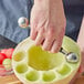 A hand using a Choice stainless steel melon baller to make melon balls.