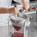 A hand pouring red liquid through a Choice stainless steel strainer.