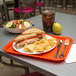 A Carlisle orange plastic fast food tray with a sandwich, chips, and a drink on it.