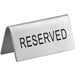 A silver stainless steel table tent sign that says "Reserved" on a table.