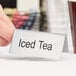 A hand placing a double sided stainless steel table tent sign that says "Iced Tea" on a table.
