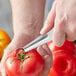 A person using a stainless steel Choice Tomato Corer to core a tomato.