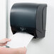 A person using a black hands-free paper roll towel dispenser.