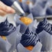 A navy blue cupcake with white frosting decorated with a silver pastry bag tip.