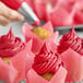 A close-up of a Chefmaster red tulip gel food coloring in a pastry bag being used to frost a cupcake.