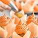 A person using Chefmaster Sunset Orange food coloring to pipe orange frosting on a cupcake.