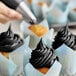 A hand uses Chefmaster Coal Black food coloring to frost a cupcake.