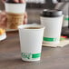 A person holding a white EcoChoice compostable paper hot cup full of brown coffee on a table.