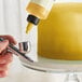 A person using a Chefmaster Metallic Gold airbrush to spray a cake.