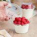 A hand holding a clear plastic parfait cup filled with raspberries and cream.