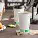 A close-up of a white EcoChoice paper hot cup on a table with coffee and croissants.