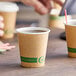 A brown EcoChoice paper hot cup with a white rim and green text sitting on a table.