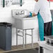 A man in a white shirt and blue apron and gloves washing a Regency stainless steel commercial sink.