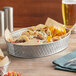 A Tablecraft stainless steel lattice oval platter with tacos and beer on a table.