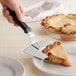 A hand using a Choice extra large black pizza pie server to cut a slice of pie.