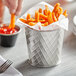A person dipping french fries into a Tablecraft lattice stainless steel fry cup.