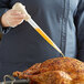 A woman using a Choice heavy-duty nylon baster to pour liquid onto a turkey.