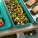 A green Cambro market pan filled with a variety of food, including green vegetables, salmon, and potatoes.
