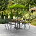 A Lancaster Table & Seating moss green umbrella over a table with chairs on an outdoor patio.