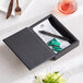 An American Metalcraft black faux leather check presenter box with a pen and a fork inside.