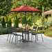 A Lancaster Table & Seating terracotta umbrella open on a patio table with chairs underneath.